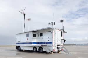 Mobile Command and Control Vehicle (C4I) with satellite communications equipment and multiple entry points, deployed for emergency response operations in an open facility