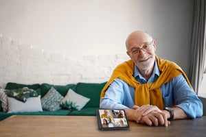 friendly-mature-man-with-gray-beard-bald-head-working-desk-from-home-smiling-with-alexa-in-video-call