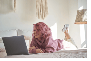 Girl laying on bed watching stream on laptop